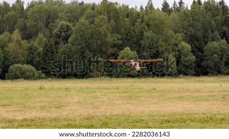 small bright yellow-red civilian small plane slows down and lands in the airfield. a propeller plane on a runway with trees in the background is landing. Royalty-Free Stock Photo #2282036143