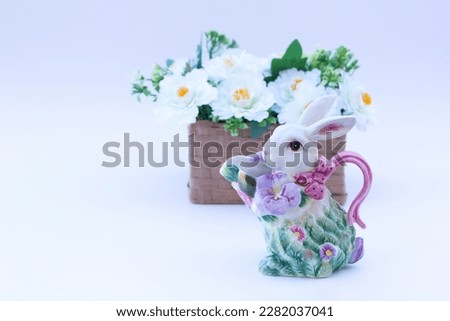 Easter decor with Colorful floral bunny-shaped ceramic saucer near the wicker little basket with white flowers on the background.