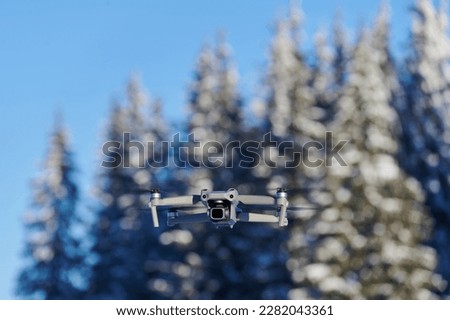 Hovering drone taking pictures of white winter nature. Drone with digital camera flying over winter forest with snow covered trees. Controlled drone taking aerial pictures.