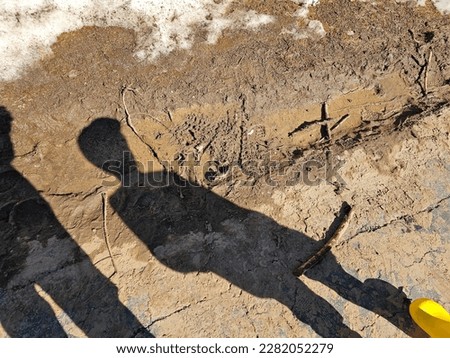The shadow of a boy standing by a muddy ditch.