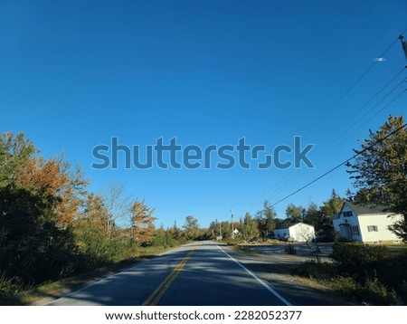 The view of a well cared for stretch of highway under a blue sky. The empty two lane highway is surrounded by vegetation on either side.