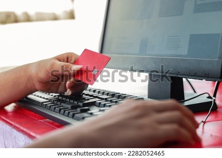a girl's hand with her credit card clutched, while looking at her computer.
