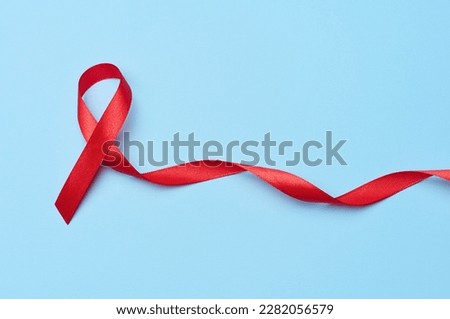 A silk red ribbon in the form of a bow is isolated on a blue background, a symbol of the fight against AIDS and a sign of solidarity and support Royalty-Free Stock Photo #2282056579