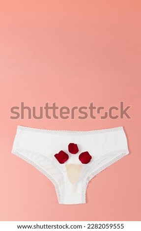 One white women's panties with a silicone menstrual cup and three red petals lie on a pink background with copy space, flat lay close-up. Woman health concept.