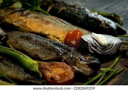 This close-up stock photo showcases a deliciously grilled trout, with mackerel and sea bass skewered in the background with lemon slices and fresh herbs. 