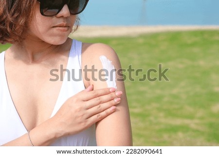 A woman is applying sunscreen and skin care to protect her skin from UV rays. She was applying sunscreen to her shoulders and arms. sunny background Health and skin care concept Royalty-Free Stock Photo #2282090641