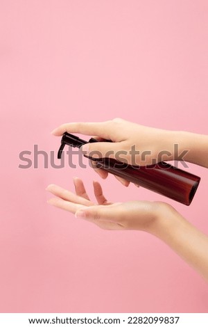 Against a light pink background, hand model is carrying a transparent pump bottle without label for cosmetic product presentation. Front view Royalty-Free Stock Photo #2282099837