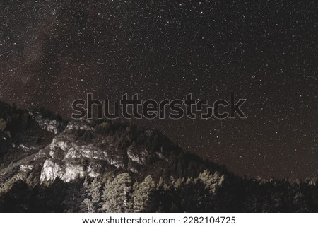 Light on a stone shore under the stars and part of the milky way on the sky at night in the dark near a mountain with trees in the Altai in Siberia.
