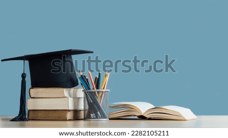 Graduation day.A mortarboard and graduation scroll on stack of books with pencils color in a pencil case on blue background.Education learning concept.