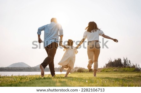 Happy family in the park sunset light. family on weekend running together in the meadow with river Parents hold the child hands.health life insurance plan concept. Royalty-Free Stock Photo #2282106713