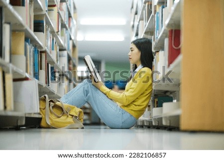 Young female college highschool student in casual clothings sitting on the floor reading book, studying and doing research for school project at a library. Learning, Education, Library concept.
