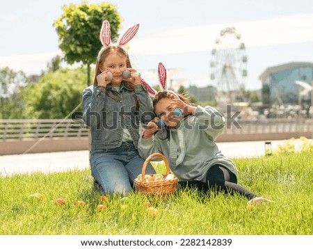 Children have fun at Easter in a sunny meadow. A red-haired girl and a brunette holding Easter eggs in her hands.