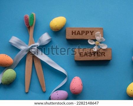 Happy Easter and dentist concept. Wooden toothbrushes with Easter decorations on blue background. Dentist Easter greating card. Top view, flat lay. Bamboo toothbrushes, colorful eggs, wooden words.