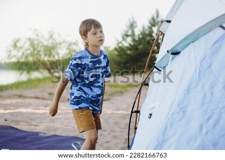 cute little caucasian boy helping to put up a tent. sunset shadows from trees. Family camping concept. High quality photo