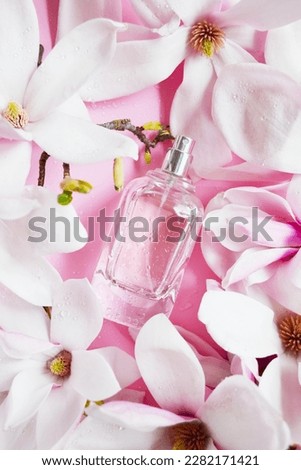 Open bottle of perfume with magnolia flowers, drops of water composition on the pink background. Fresh magnolia aroma. Idea of sweet pure smell of flowers for young girls.  