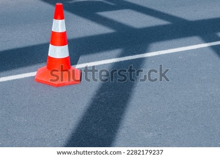 A bright red traffic cone stands alone on an asphalt city street, warning drivers of potential hazards ahead with its security symbol.