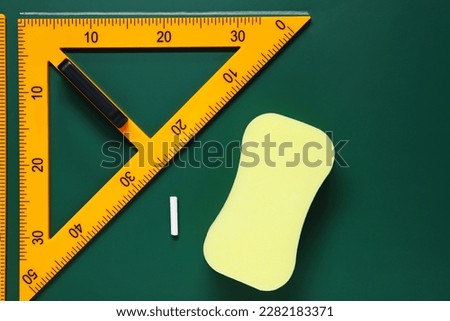 Protractor, sponge, chalk and ruler on green chalkboard, flat lay