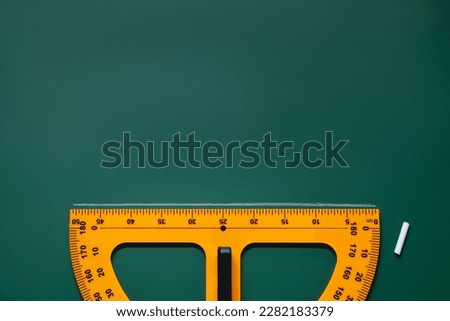 Yellow protractor and chalk on green chalkboard, flat lay. Space for text