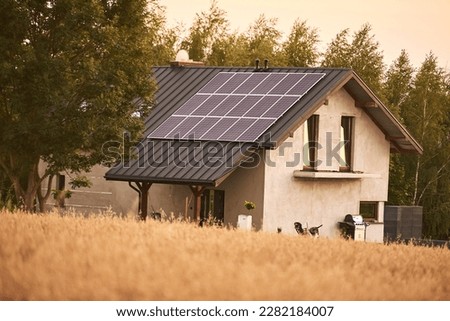 Photovoltaic panels on a newly built house located behind a field of mature wheat. Royalty-Free Stock Photo #2282184007