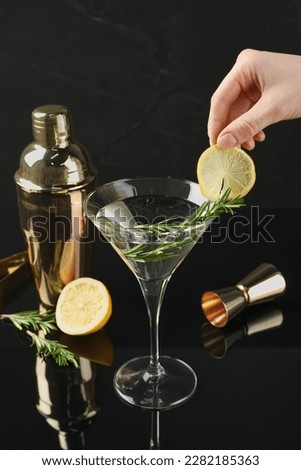 Woman decorating Martini cocktail with lemon slice on black background, closeup