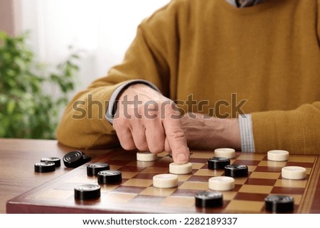 Playing checkers. Senior man thinking about next move at table in room, closeup