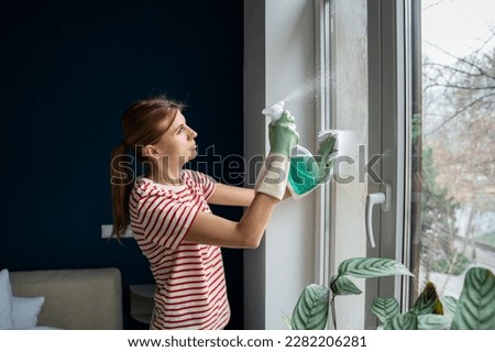 Attentive woman wash glass window wearing rubber protective gloves, with rag and eco spray bottle detergent. Focused professional maid cleaning hotel room. Housekeeping perfect tidiness domestic work Royalty-Free Stock Photo #2282206281