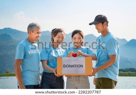 volunteers team gathering for charity foundation in the park by the pond, carrying donation boxes and a red heart for campaign to collect donation items