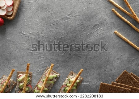 Food photography. Delicious rye crispbreads with cream cheese, cucumber, radish and breadsticks on light grey textured table, flat lay with space for text