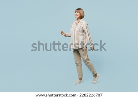 Full body side profile view smiling happy elderly woman 50s years old wear shirt walking going strolling isolated on plain pastel light blue cyan color background studio portrait. Lifestyle concept Royalty-Free Stock Photo #2282226787