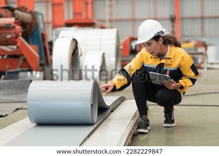 Metalwork manufacturing, warehouse of raw materials. Female factory worker inspecting quality rolls of metal sheet in factory during manufacturing process, wearing safety uniform, use digital tablet