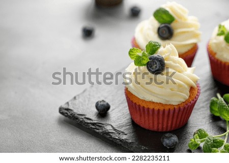 Cupcakes, muffins decorated with cream, berries and green mint leaves on dark slate cutting board. Delicious homemade dessert. Pastry.