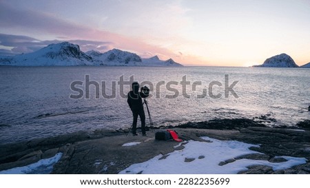 The photographer take a picture of Lofoten islands in winter. A male uses camera and tripod to capture a beautiful landscape picture at twilight in Lofoten. Majestic view of Haukland Beach. 