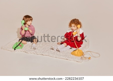 Two cute children, sister and brother sitting on floor and playing together isolated over grey background. Concept of happy childhood, leisure activities, fun, lifestyle, family, retro style Royalty-Free Stock Photo #2282236107