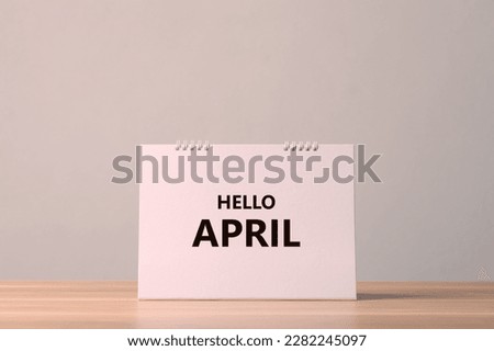 Start to new month concept, Paper desk calendar with text HELLO APRIL on the top of wooden table with grey color wall background. Studio shot.