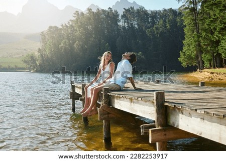 Young couple, lake and jetty with laughing, happiness and bonding with love in nature for holiday. Man, woman and comic joke on bridge by water to relax with conversation, care and vacation in summer Royalty-Free Stock Photo #2282253917