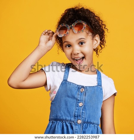 Girl child, smile and sunglasses in studio portrait for summer style or happy by yellow background. Mixed race model, female kid or fashion frame on face for surprise expression, eye care and youth