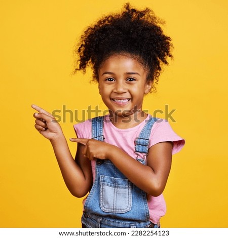 Portrait, studio and happy child pointing hand at space with a smile on face on yellow background. Young girl kid with happiness, carefree and positive attitude to show product placement mockup deal Royalty-Free Stock Photo #2282254123