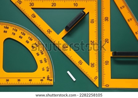 Protractor, triangles and chalk on green chalkboard, flat lay