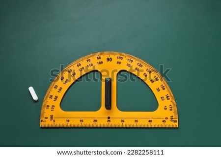 Yellow protractor and chalk on green chalkboard, flat lay. Space for text