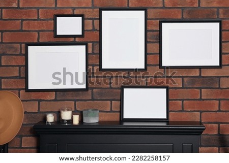 Empty frames and scented candles on fireplace indoors