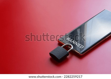 Modern mobile phone is a smartphone with the inscription "banned" and padlock on a red background. Concept of a ban on the use of smartphone, cellular communication and gadgets. Close-up Royalty-Free Stock Photo #2282259217