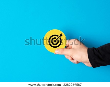 Goal achievement, setting the business objectives. Personal or business vision. Male hand holding a yellow circle sign with target goal symbol against blue background. Royalty-Free Stock Photo #2282269587