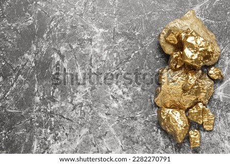 Pile of shiny gold nuggets on grey table, flat lay. Space for text