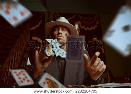 The criminal world of the mafia. A tough gangster man in an elegant black suit and a white hat sits in a luxury apartment and plays cards. Retro style. Detective movie. Royalty-Free Stock Photo #2282284705