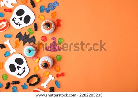 Tasty candies and Halloween decorations on orange background, flat lay. Space for text