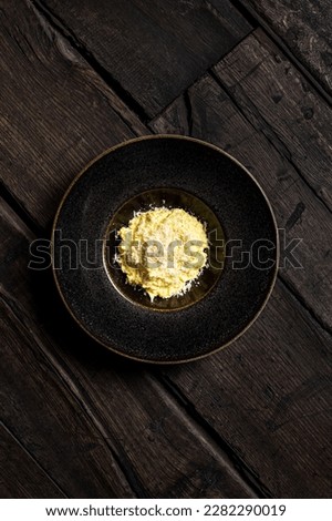 Corn porridge Mamaliga with goat cheese and pieces of pork bacon in a dark ceramic plate with wide margins on dark wooden boards.