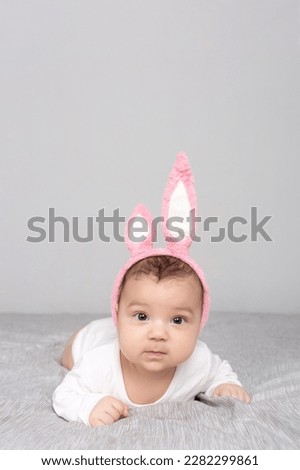 Baby with rabbit ears lies on a gray light bed. The concept of a Happy Easter. Mockup for advertising, design, celebration, postcards. Copy space.