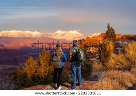 Couple enjoying beautiful sunset in winter in the mountains in Utah. Friends relaxing on hiking trip. Canyonlands National Park at sunset against snow covered mountains. Utah, USA. Royalty-Free Stock Photo #2282301851