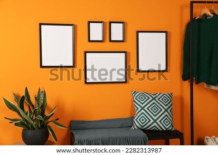 Empty frames hanging on orange wall in stylish room. Mockup for design