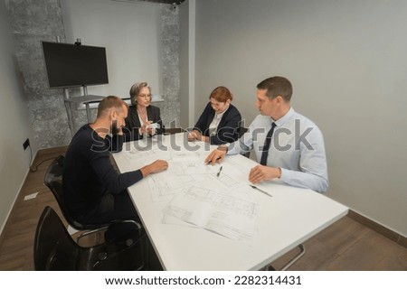 Four business people sitting around a table discussing blueprints. Designers engineers at a meeting. 